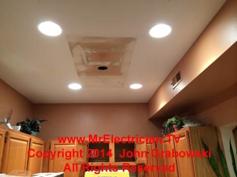Recessed lights in a condominium kitchen with a hole in the ceiling from the old ceiling electrical box that powered the old light fixture