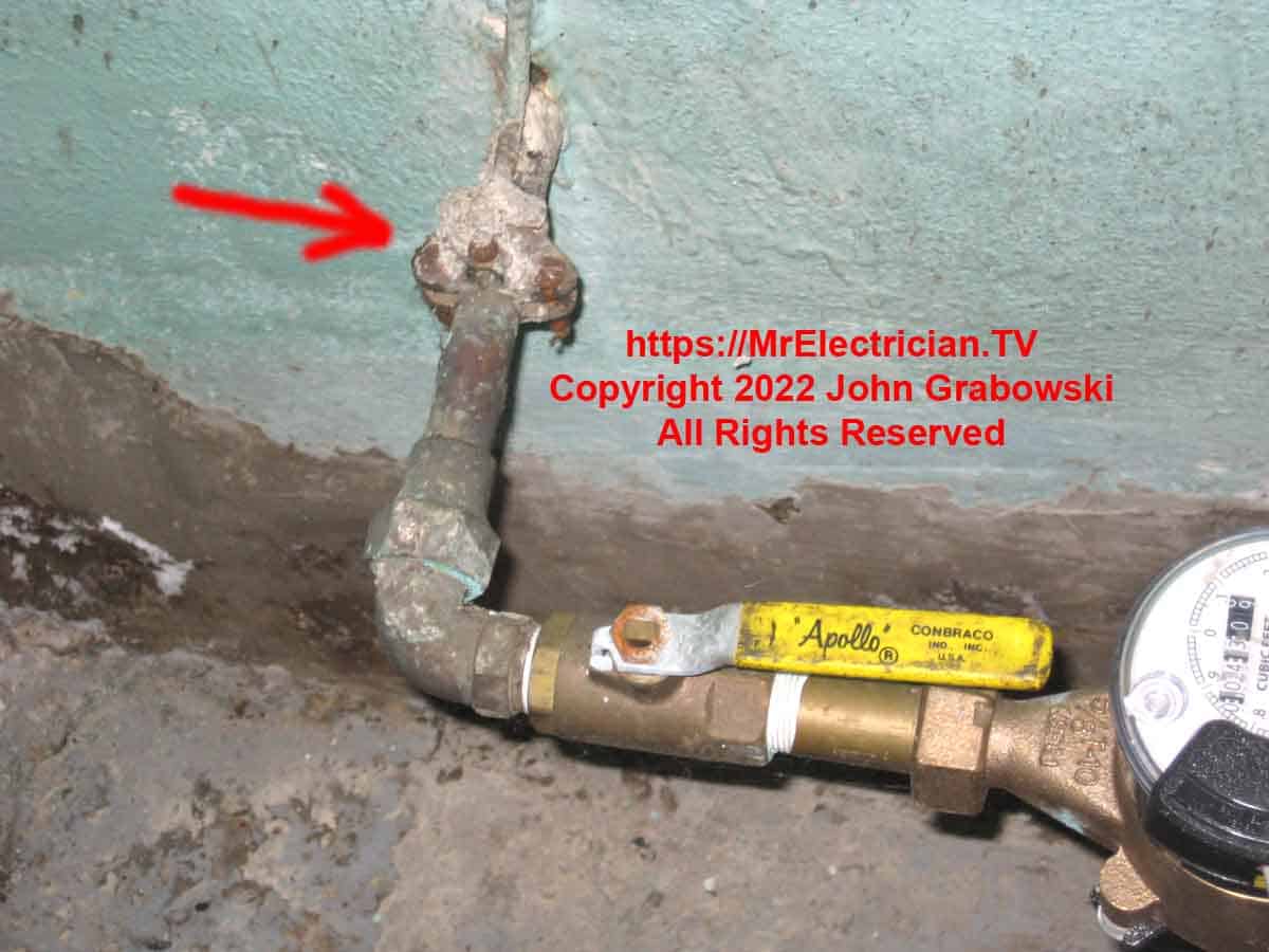 A photo of a corroded water pipe ground clamp attached to the water service pipe before the water meter in a basement