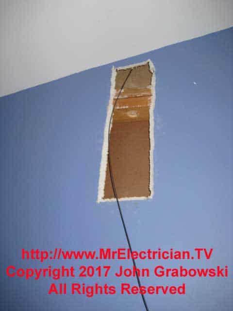 A metal fish tape is used here to pull a wire through from the ceiling down into the wall.