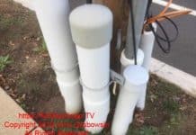 Five inch and four inch PVC electrical conduit emerging from the ground. Conduits are attached to a wood utility company power pole and are for the electrical and telephone service for a building
