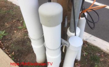 Five inch and four inch PVC electrical conduit emerging from the ground. Conduits are attached to a wood utility company power pole and are for the electrical and telephone service for a building