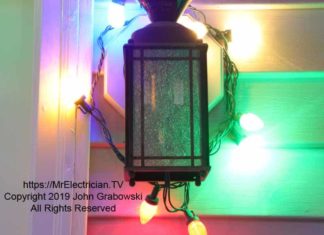 An outdoor light fixture with Christmas lights wrapped around it and plugged into the light bulb socket and energized