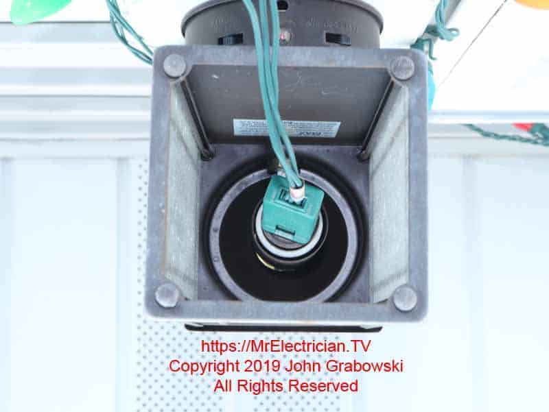 Inside of an outdoor light fixture with a cord for Christmas lights plugged into the light bulb socket
