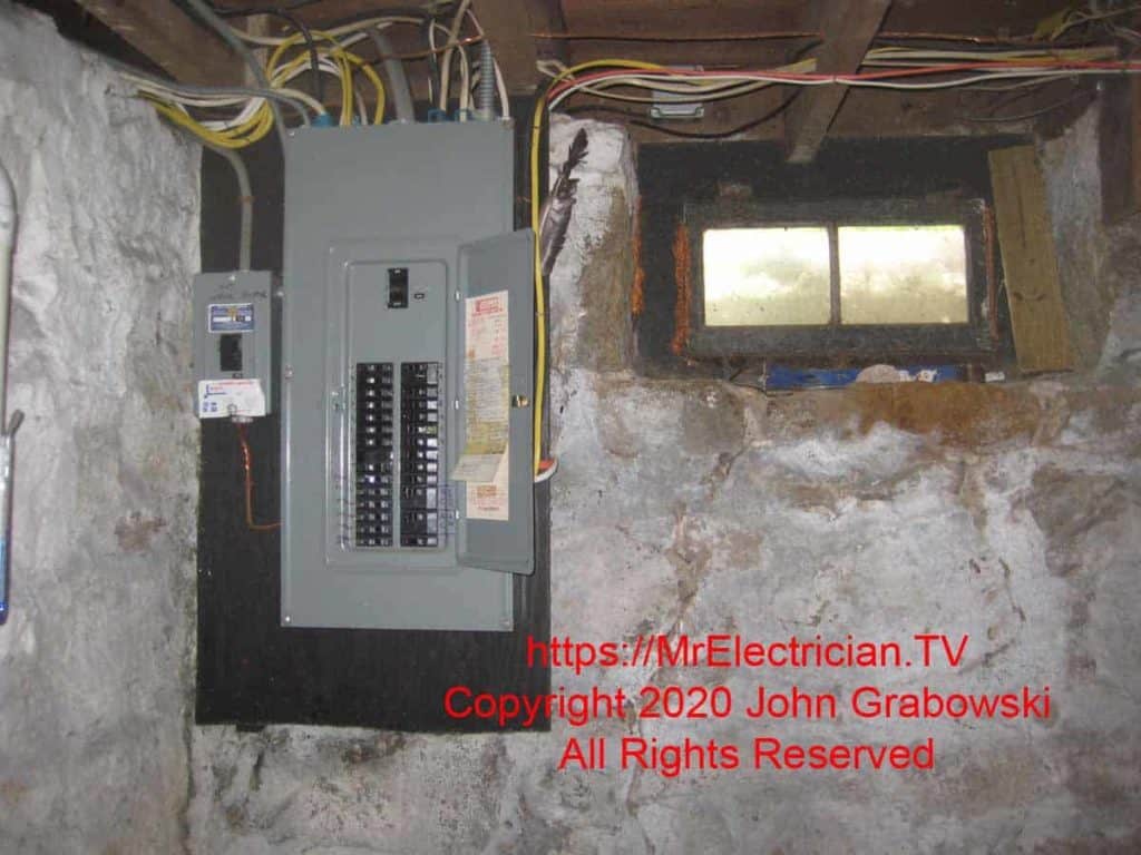 Wide shot of the main electrical panel with the cover on. To the left of the main panel is a circuit breaker in a separate load center for the water heater