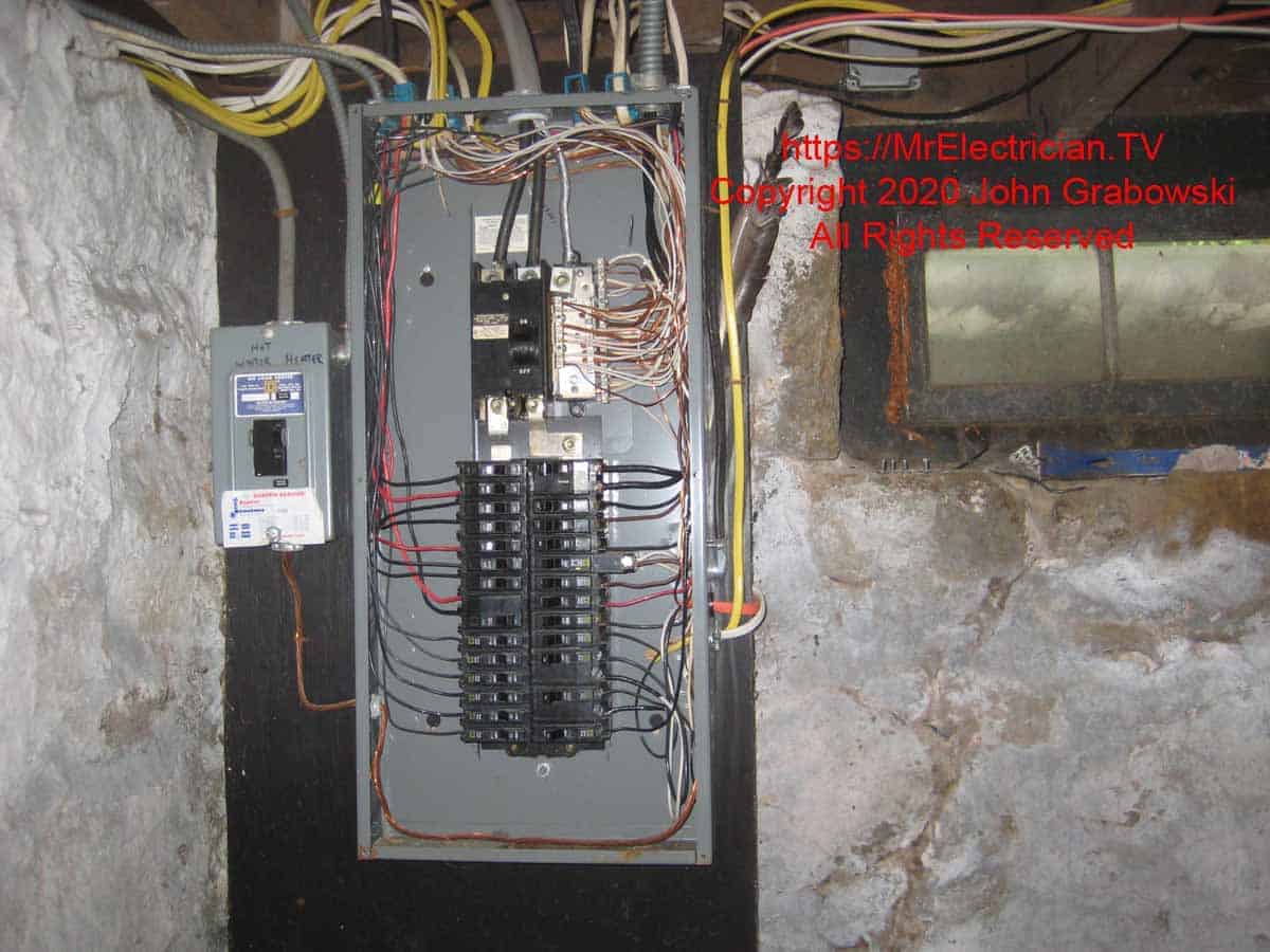 Wide shot of the main electrical panel with the cover removed showing the existing circuits. To the left of the main panel is a circuit breaker in a separate load center for the water heater which was connected to its own electric meter