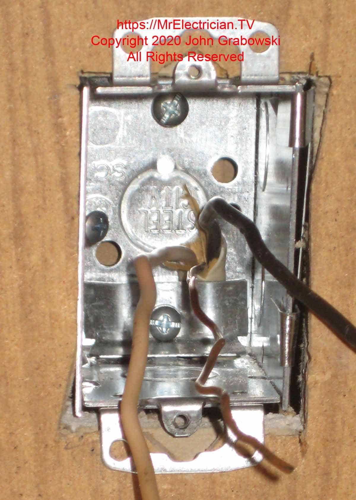 A one gang metal outlet box mounted to the wall with one Madison Bar and one #8 sheet metal screw. The 12/2 cable is entering from the bottom under the cable clamp. The upper cable clamp has been removed and the clamp screw has been reinstalled for grounding the box