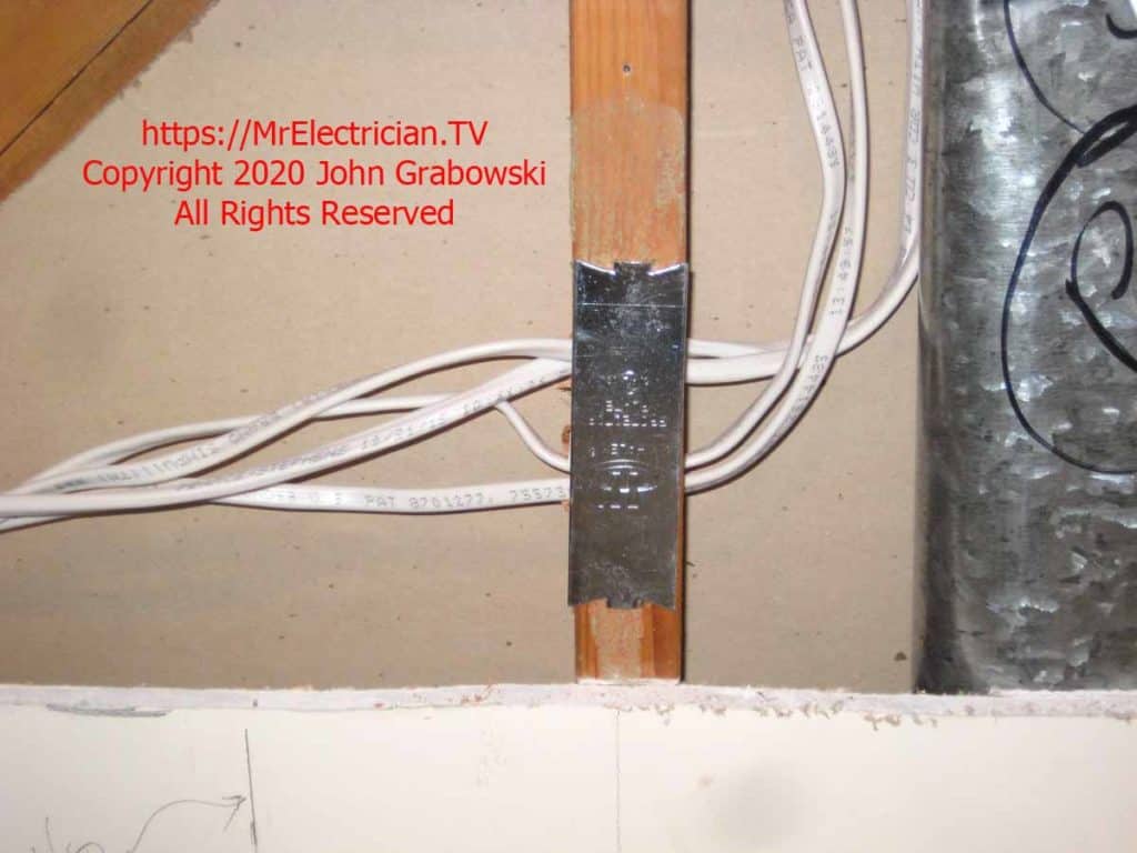 Some Romex cables passing through a wood wall stud that has a steel protector plate fastened to its surface.