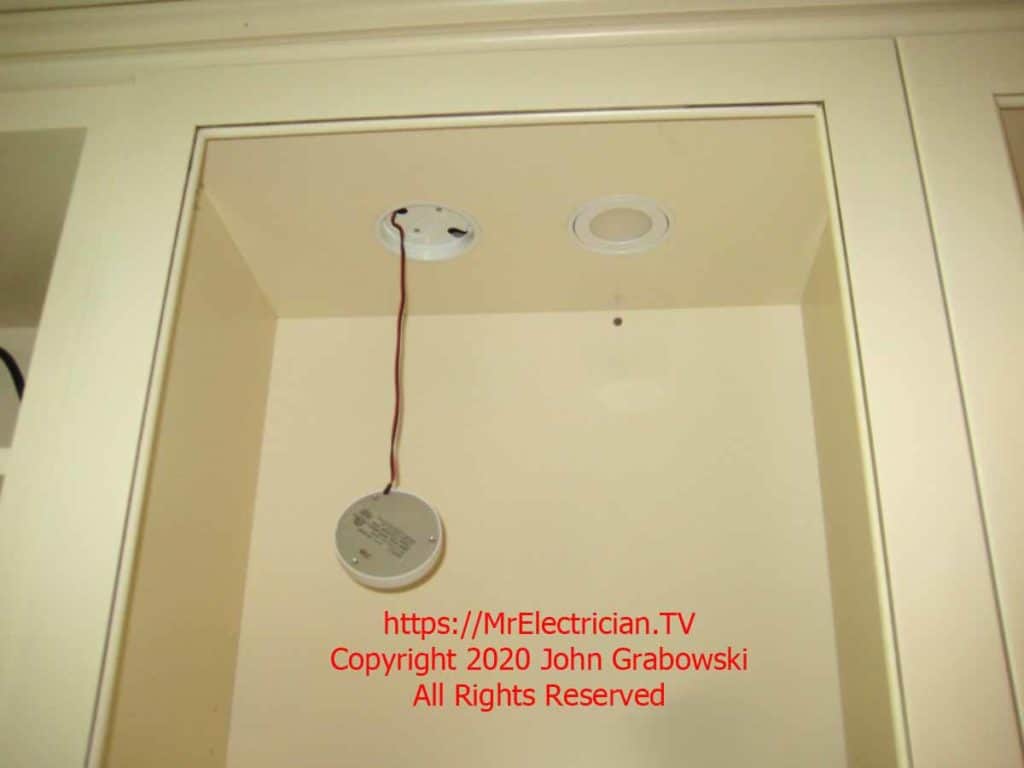 Two low voltage recessed lights inside of a kitchen cabinet, one light is hanging by a wire