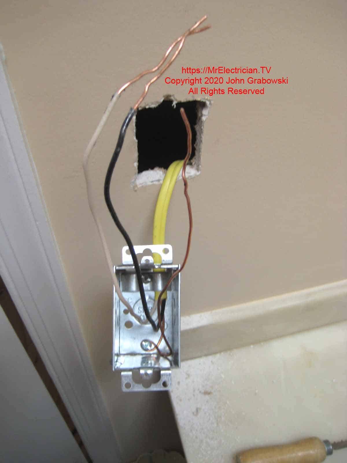 Metal electrical outlet box hanging from hole in wall with wire attached