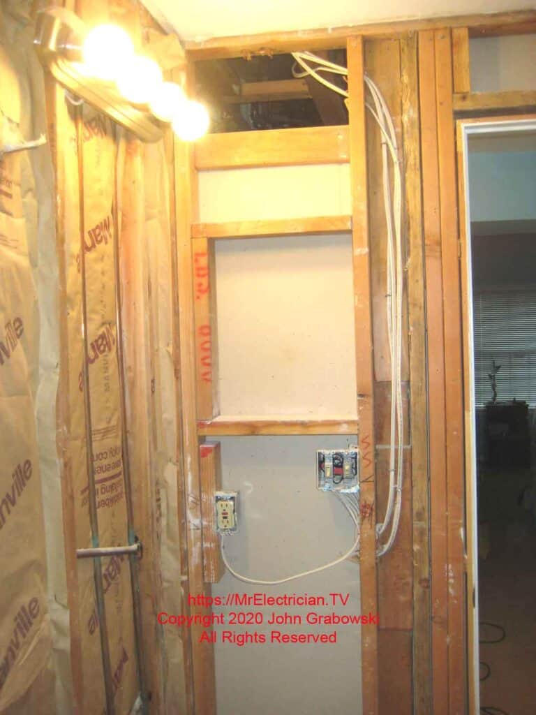 An exposed bathroom wall during remodeling reveals the wiring route around the medicine cabinet