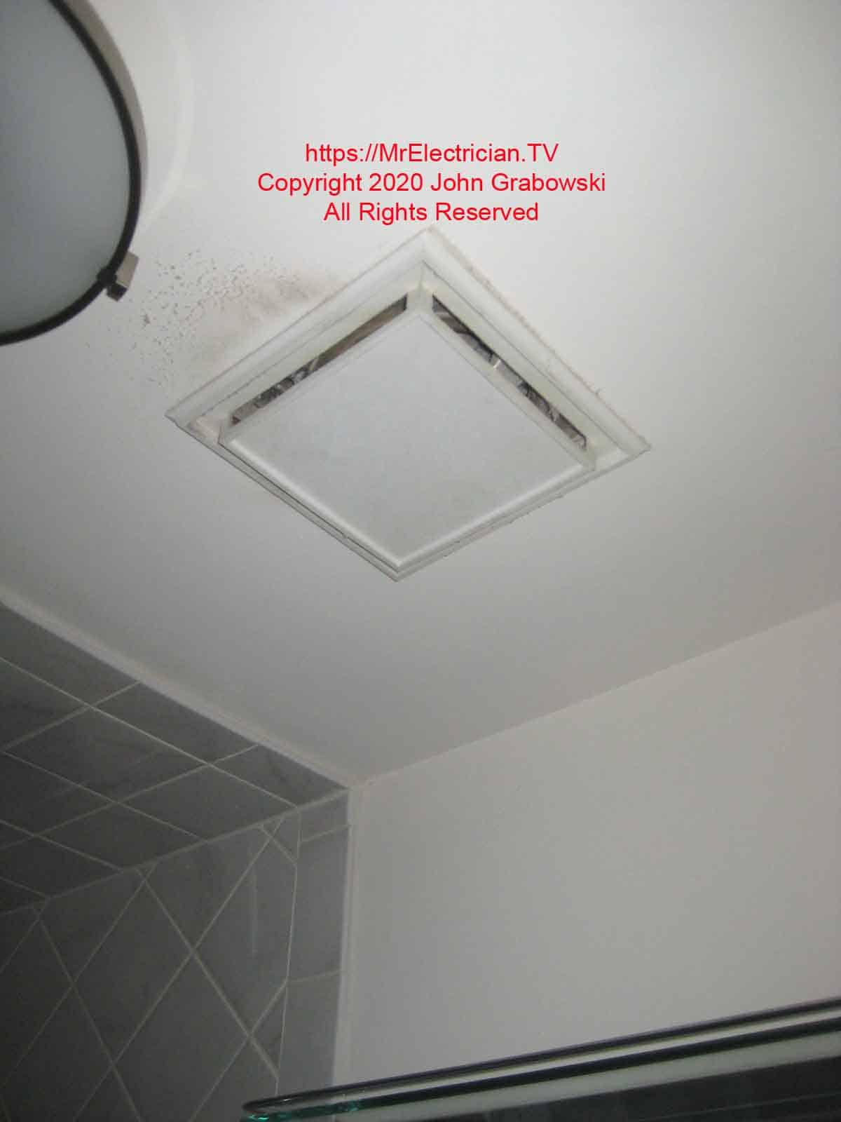 Old bathroom exhaust fan next to ceiling light fixture