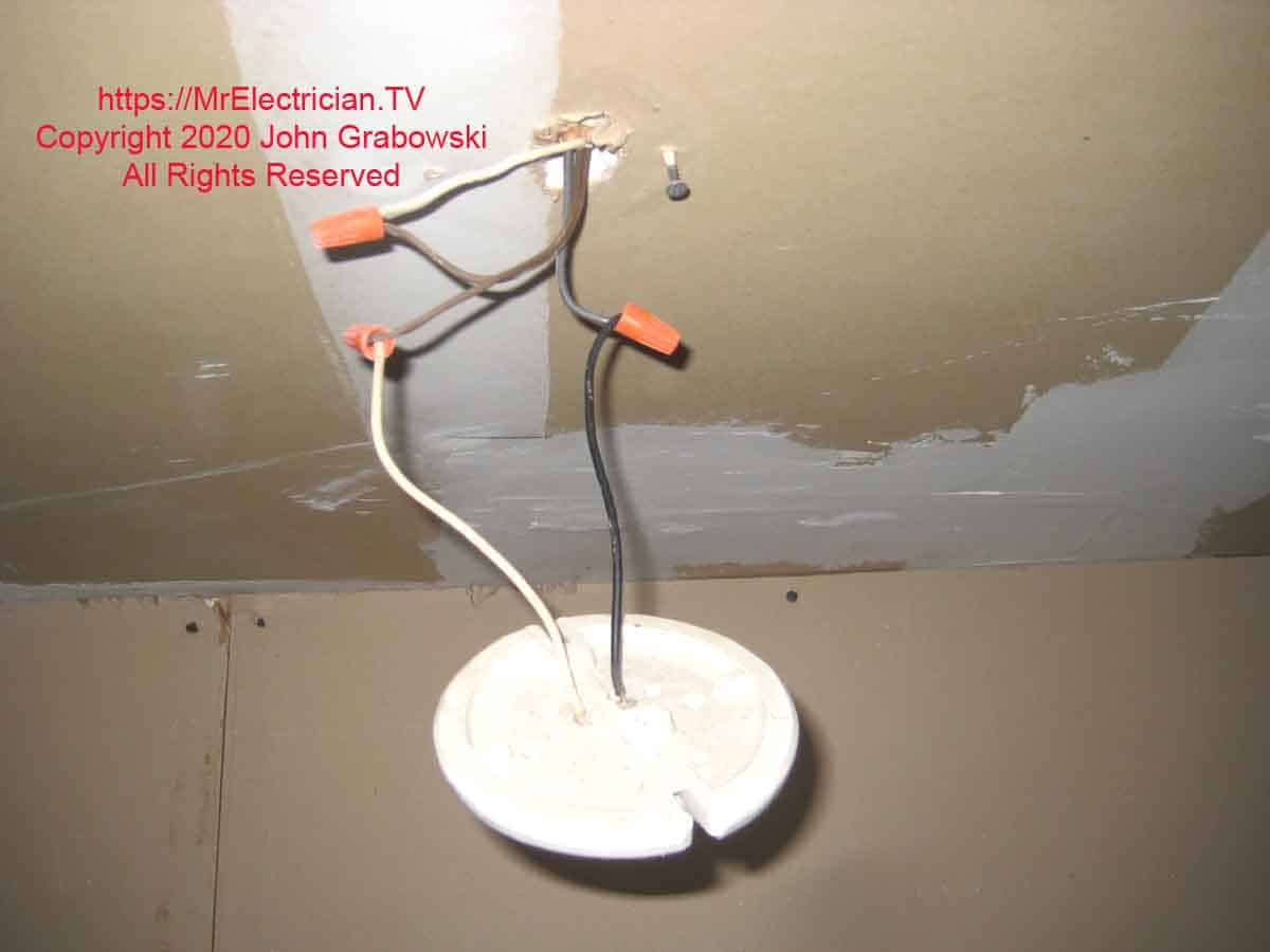 A porcelain keyless light socket hanging by wires without an electrical box and improper wiring used.