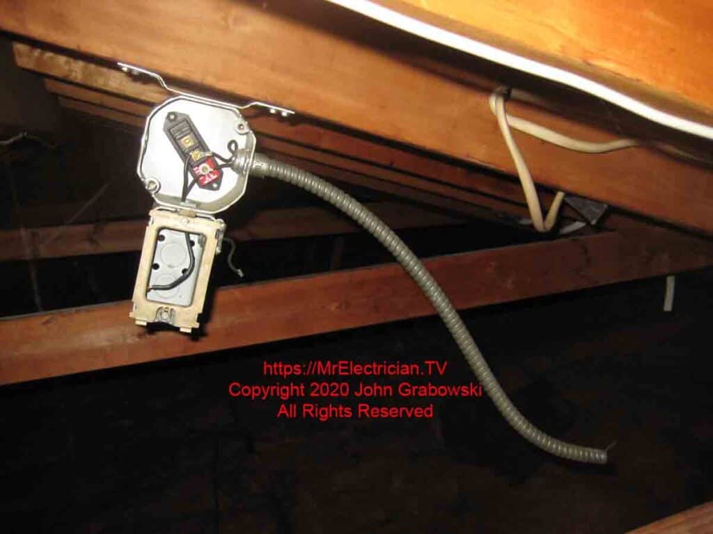 An old fan thermostat not connected to anything hanging on the underside of a roof joist.