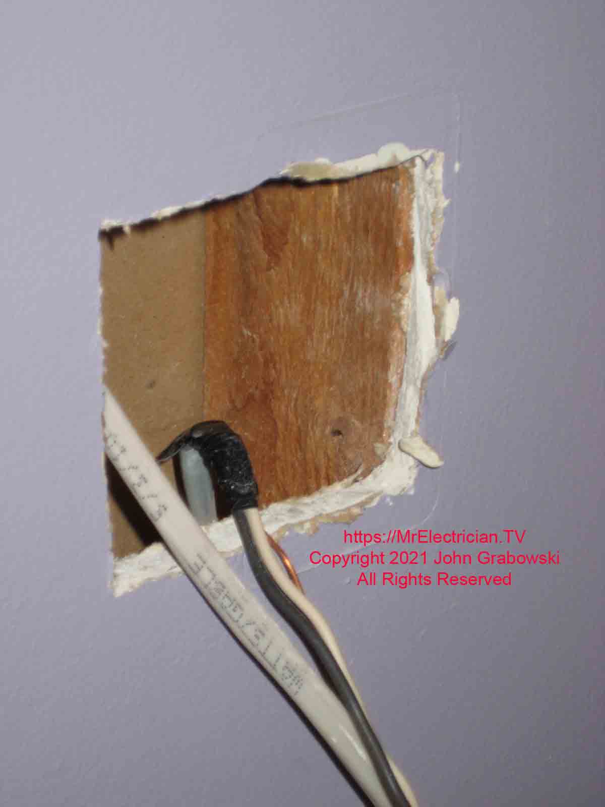 Newly enlarged hole with wires protruding for a two gang old work electrical switch box