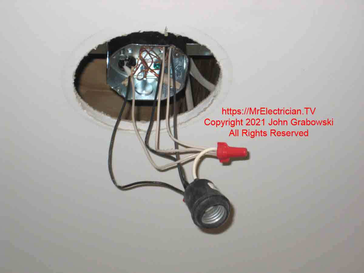 A pigtail light socket hanging from a ceiling fan box installed in a hole formerly occupied by a six-inch diameter recessed light fixture.
