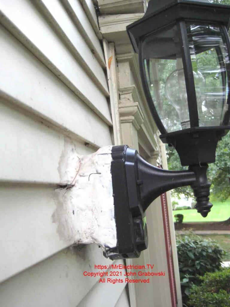 Side view of an outdoor luminaire mounted to an indoor electrical box that is covered with duct tape and caulk.