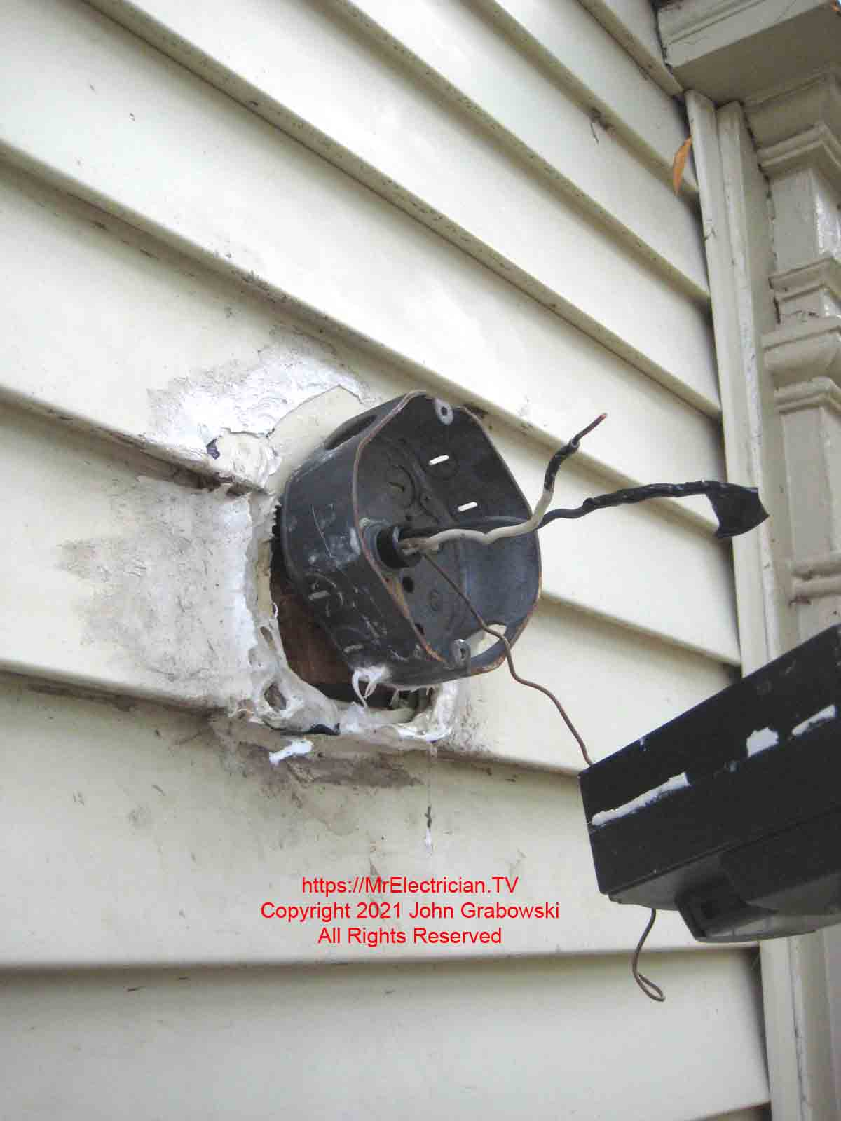 The old light fixture, duct tape, and caulk is removed to reveal an indoor electrical box with some of the knockouts removed