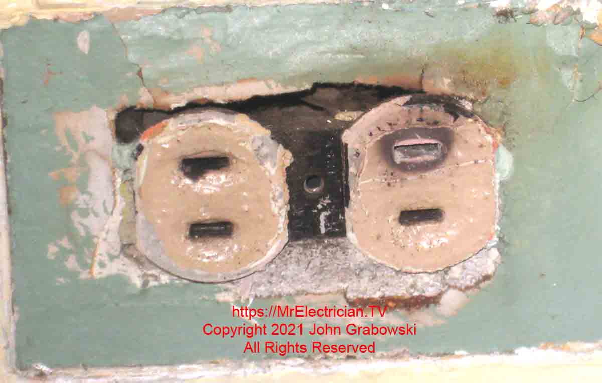 A very old and painted over two wire ungrounded electrical outlet with a burned hole