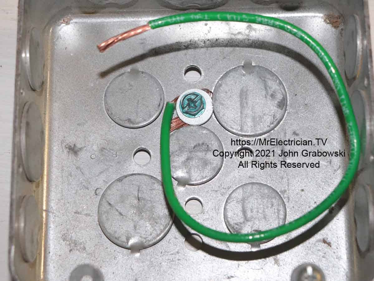 A stranded wire grounding pigtail under a washer with a green screw