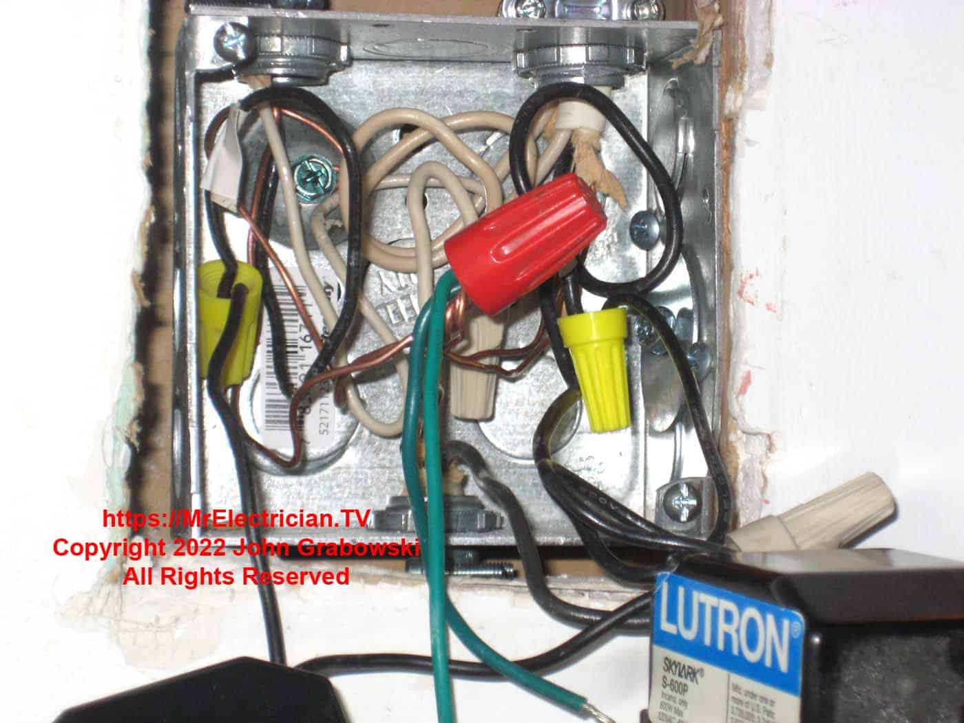 A four inch square metal electrical box in a wall with wires