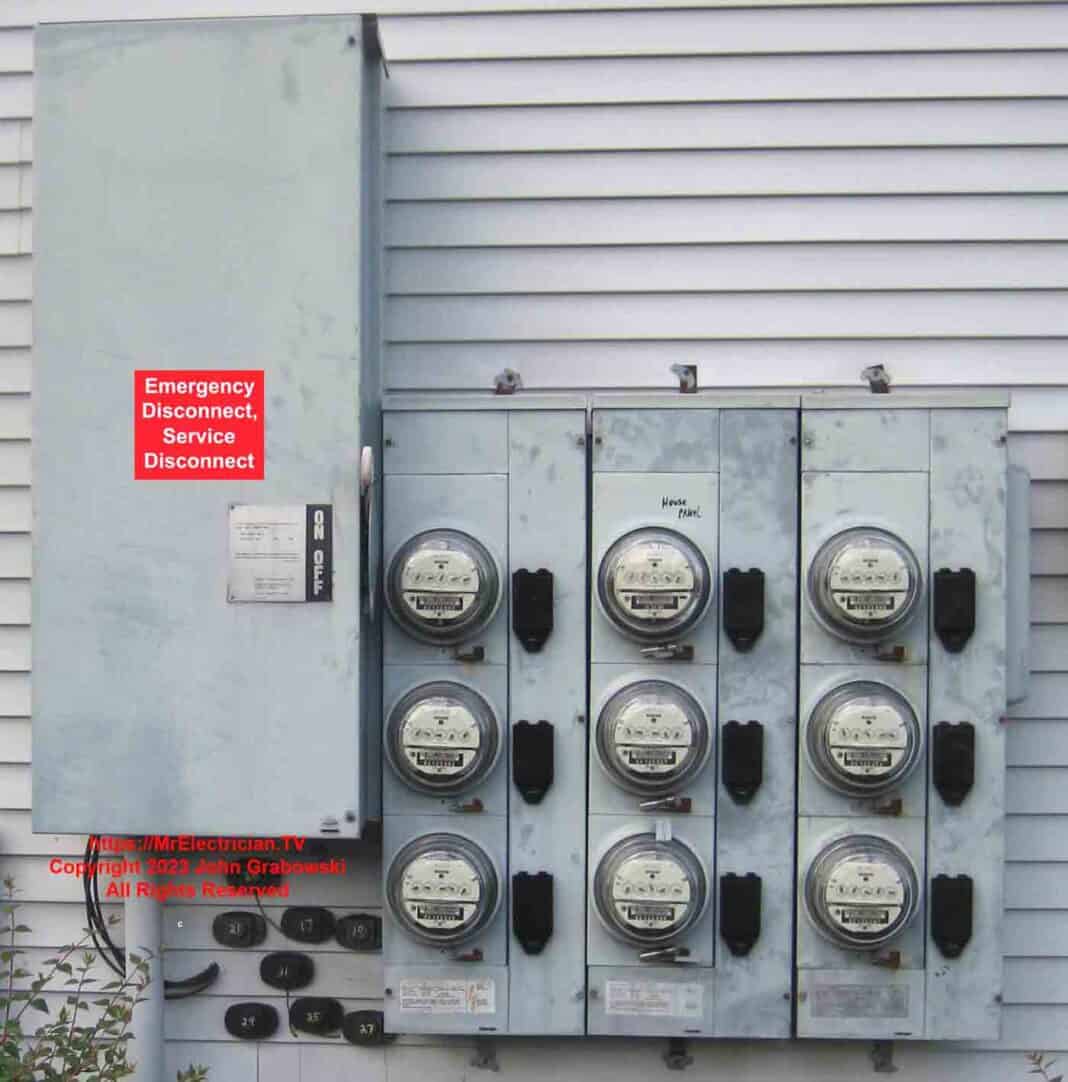 A nine-gang electric meter stack with a large disconnect switch for all. There is a red sticker with white letters on the front of the large disconnect switch that reads: 