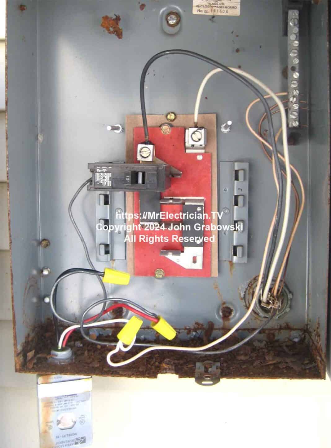 The interior of an active outdoor electrical panel with a white wire being used as one of the LINE conductors feeding the panel. The equipment grounding conductor is being used as a neutral which can cause phantom voltage.