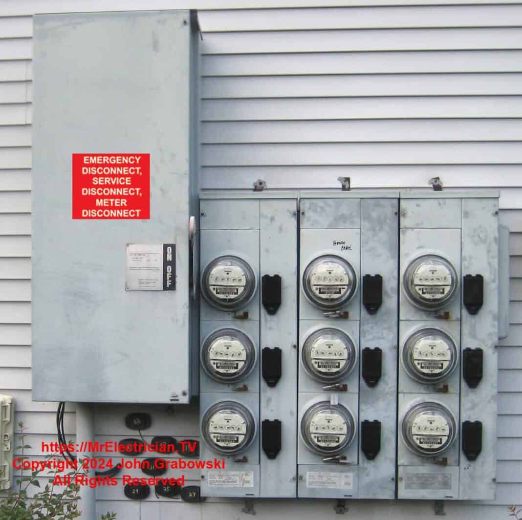A main electric disconnect switch connected to nine electric meters attached to the side of a residential building. The disconnect switch is labeled Emergency Disconnect, Service Disconnect, Meter Disconnect.