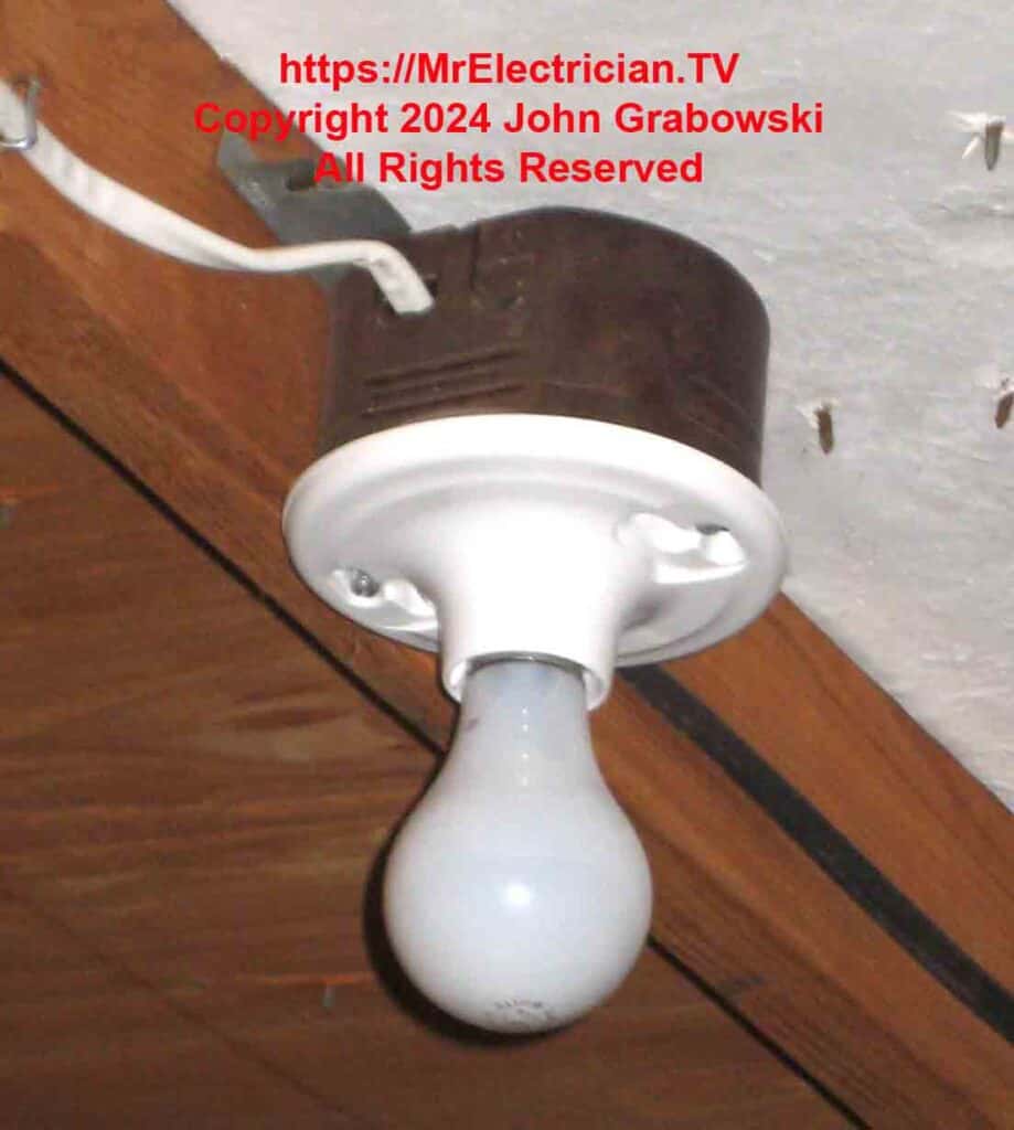 A white plastic lamp-holder is attached to a brown plastic electrical box as an attic light. The white two-wire cable from the switch is going into the side of the box.