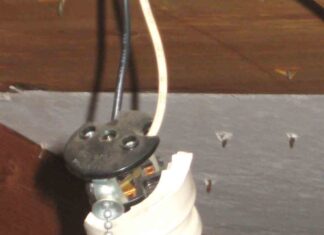 A close shot of a broken light bulb socket with a pull chain hanging by two electrical wires in an attic.