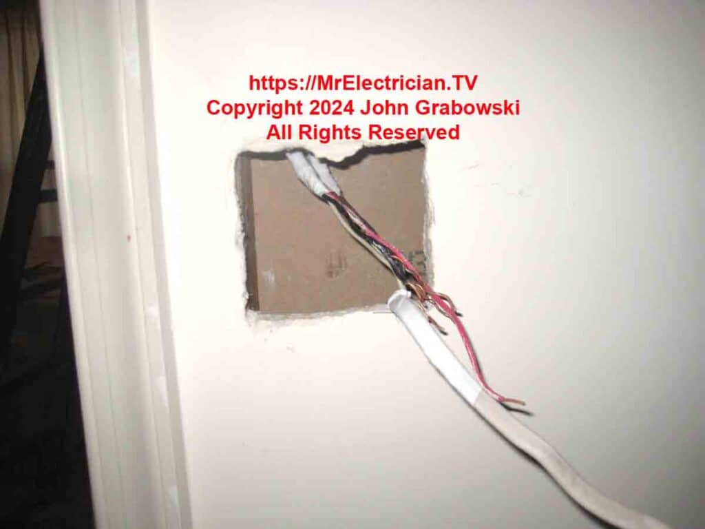 Wires hanging out of a hole cut in a wall for a two gang electrical box to be installed.