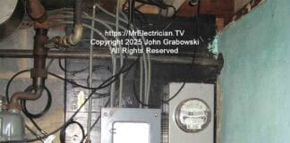 An older electric meter and fuse box located inside a basement adjacent to the foundation wall. The armored grounding electrode conductor is coming out of the bottom of the meter socket.