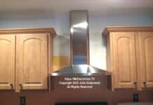 The finished installation of a kitchen chimney hood between cabinets and over an existing stove