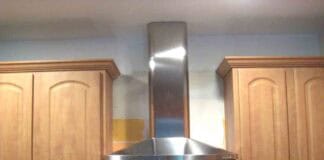The finished installation of a kitchen chimney hood between cabinets and over an existing stove