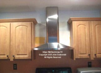 The finished installation of a kitchen chimney hood between cabinets and over an existing stove