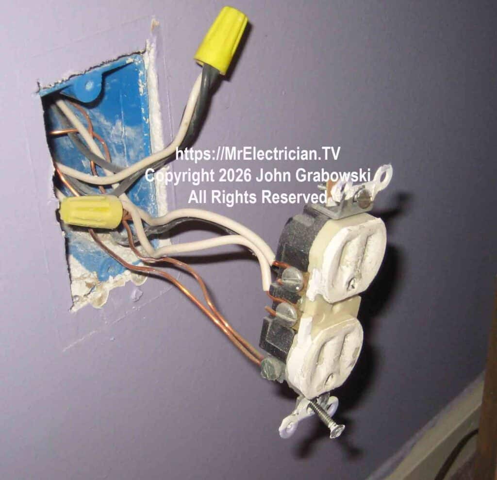 An ivory electrical receptacle with a painted face is hanging by a black wire, two white wires, and two bare copper wires. There is a yellow wirenut at the top of the photo with two black wires and one white wire joined together. That white wire is the LINE wire for the wall switch that controls this outlet.