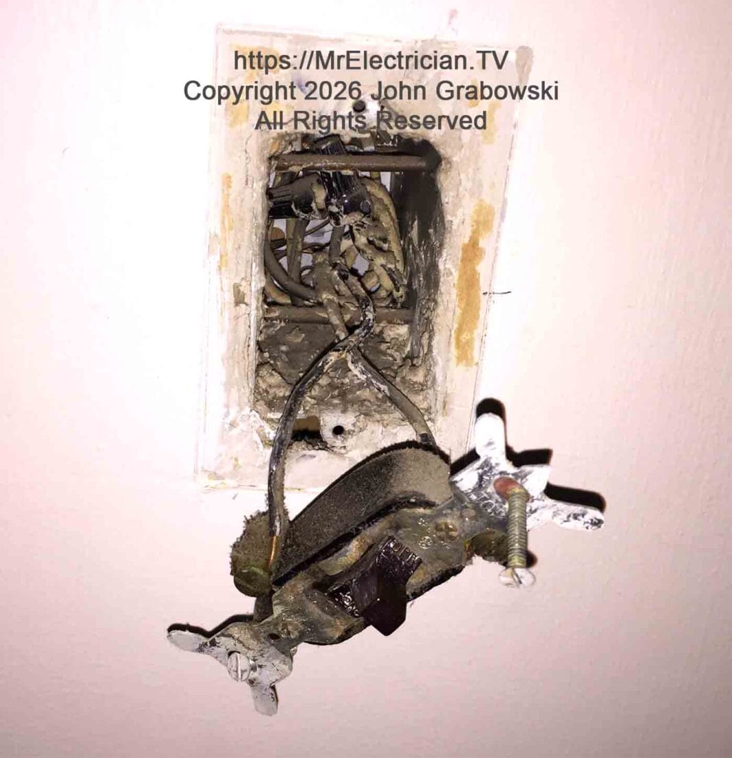 A photo of an old single pole light switch hanging from the electrical switch box by some older wires