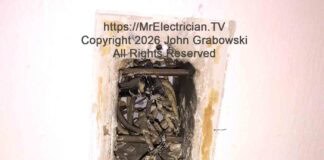 A photo of an old single pole light switch hanging from the electrical switch box by some older wires